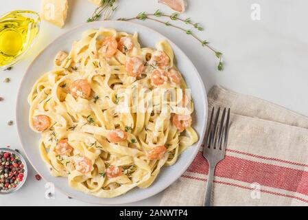 La pasta italiana Le fettuccine o tagliatelle con gamberi in una salsa cremosa con parmigiano e timo in una piastra su marmo bianco tavola. vista superiore Foto Stock
