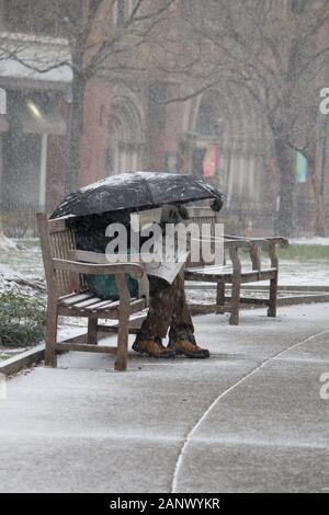 Philadelphia, PA, Stati Uniti d'America - 18 Gennaio 2020: un uomo si siede su una panchina nel parco leggendo un giornale sotto il suo ombrello in Rittenhouse Square park durante la città Foto Stock