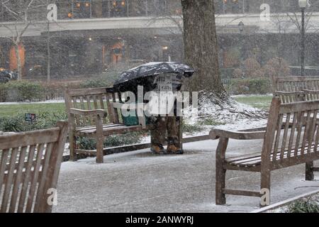 Philadelphia, PA, Stati Uniti d'America - 18 Gennaio 2020: un uomo si siede su una panchina nel parco leggendo un giornale sotto il suo ombrello in Rittenhouse Square park durante la città Foto Stock