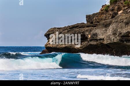 Le onde a una spiaggia segreta, Nusa Ceningan, Bali, Indonsia. Scogliera di roccia in background. Cielo blu in distanza. Foto Stock