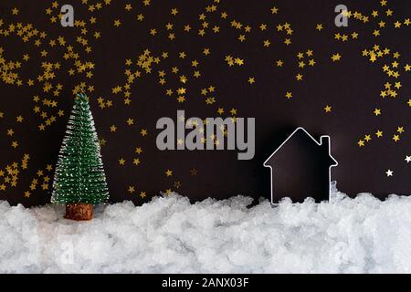 Natale in miniatura e casa sulla neve e uno sfondo scuro con stelle luccicanti con copia spazio. Composizione di natale, modello di cartolina Foto Stock