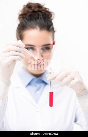 Giovane medico o farmacista aggiungendo liquido rosso nella beuta con un nuovo vaccino Foto Stock