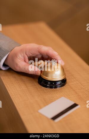 Mano di imprenditore contemporaneo sopra l'anello pulsante sul banco della reception in legno Foto Stock