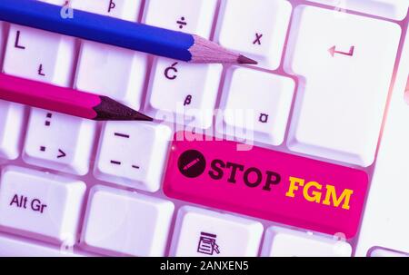 La grafia la scrittura di testo Stop fgm. Foto concettuale di porre fine o di arresto sul taglio genitale e la circoncisione White tastiera PC con nota vuota abo della carta Foto Stock