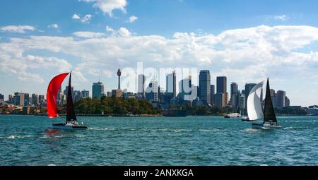 L'iconico skyline di Sydney è incorniciato da due barche a vela colorate che navigano nello splendido porto della città Foto Stock