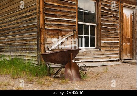 MT00395-00...MONTANA - Vecchia carriola e la pala al di fuori di uno degli edifici più antichi conservati presso la città fantasma di Bannack in stato di Bannack Park. Foto Stock