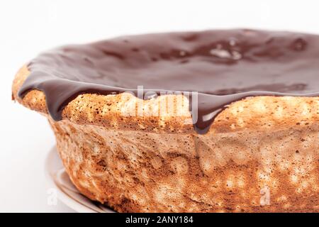 Il cioccolato che scorre sui lati della torta di pan di spagna con caramello versando attorno ai bordi su sfondo bianco vicino. Foto Stock