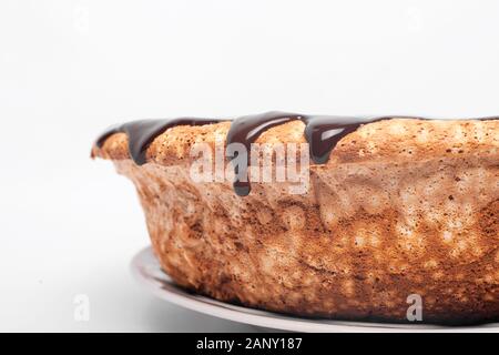 Il cioccolato che scorre sui lati della torta di pan di spagna con caramello versando attorno ai bordi su sfondo bianco vicino. Foto Stock