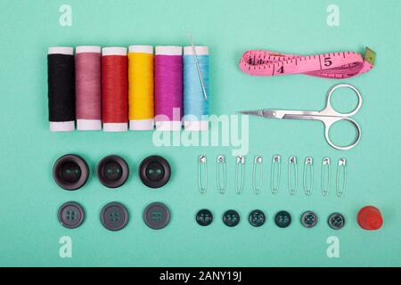 Kit di cucitura accessori.Impostare gli strumenti per il cucito e i fili colorati,aghi,perni,forbici su sfondo verde vista dall'alto. Foto Stock