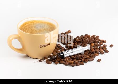 Una tazza di caffè, chicchi di caffè e una siringa. Concetto di dipendenza da caffè. Foto Stock