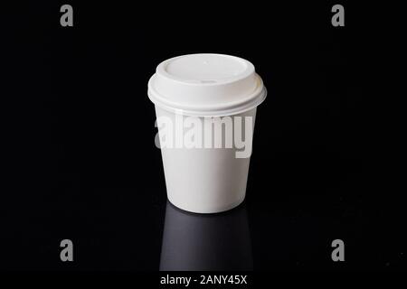 Bianco cartone monouso tazza da caffè con coperchio in plastica su uno sfondo nero. Foto Stock