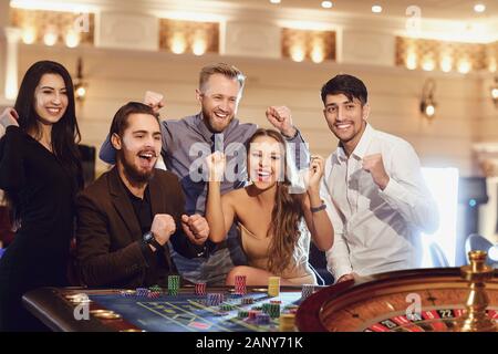 Allegro gruppo di amici gode di vincere alla roulette poker in un casinò. Foto Stock