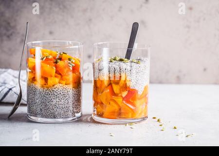 Budino di Chia con persimmon e i semi di zucca in bicchieri e sfondo grigio. Sano cibo vegan concetto. Foto Stock