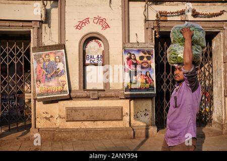 Un uomo che porta borse di verdure sulla sua testa passando il Palace Talkies, un cinema a Byculla, Mumbai, India, poster di una lingua Bhojpuri esposto Foto Stock