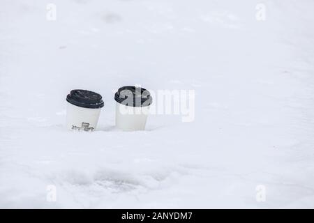 Caffè usa e getta bicchieri di carta nella neve. il cestino in città. Foto Stock