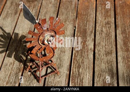 Colpo ad angolo alto di un piccolo mulino a vento arrugginito su un superficie in legno Foto Stock