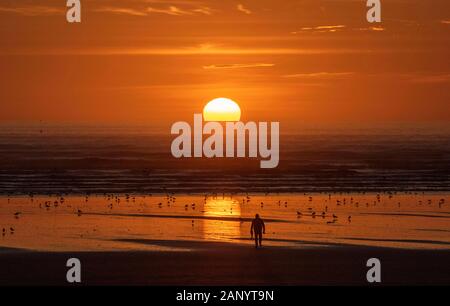 Un uomo cammina verso la spettacolare tramonto a Cefn Sidan spiaggia vicino a Llanelli in Carmarthenshire questo pomeriggio. Foto Stock