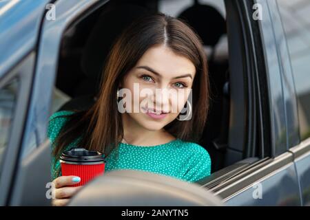 Con successo una donna si siede in una vettura e beve caffè caldo. Il concetto di trasporto, diritto di guidare, business donna e assicurazione. Foto Stock