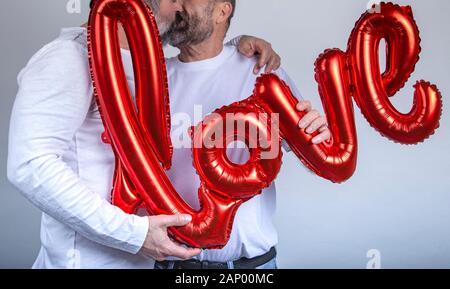 Coppia gay kissing tenendo un palloncino rosso con la parola amore su sfondo bianco. Il giorno di San Valentino concetto Foto Stock