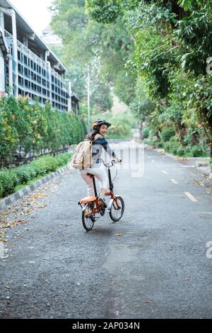 sorridente giovane donna asiatica che indossa casco e borsa cavalcare la sua bicicletta pieghevole Foto Stock