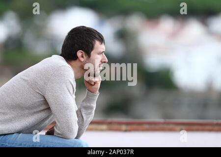 Uomo preoccupati pensando che guarda lontano seduta su una panchina da solo in una città Foto Stock