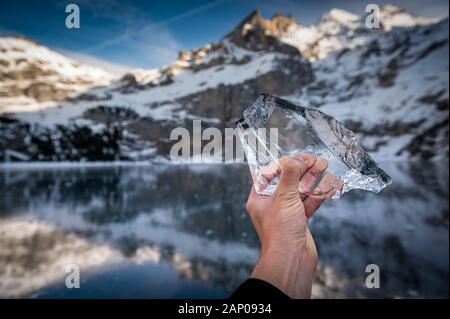 Mano che tiene una bella cancella pezzo di ghiaccio sul lago ghiacciato Oeschinensee con la riflessione e la montagna Blümlisalp in Berner Oberland Foto Stock