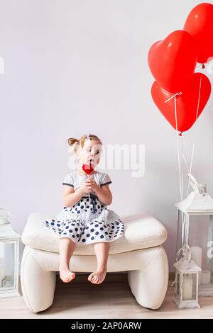 Adorabile ragazza bionda di mangiare un lecca-lecca di caramello. Bambina azienda alla bocca per lecca-lecca di caramello a forma di cuore. Il giorno di San Valentino del concetto. Foto Stock