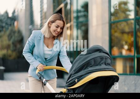 Ritratto di una donna d'affari di successo in tuta blu con il bambino. Business donna spingendo passeggino Foto Stock