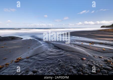 Spiaggia con sabbia scura e alcune rocce in primo piano le nervature di sabbia, che si sono formati da un piccolo fiume, alcuni ciuffi di fasci giacciono sulla sabbia, girato da d Foto Stock