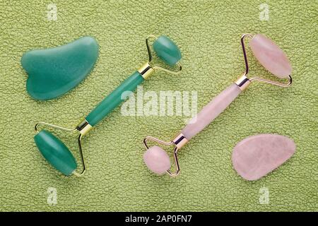 Real jade rullo del viso e quarzo rosa su sfondo verde con pietre Massaggio gua sha, laici piatta Foto Stock