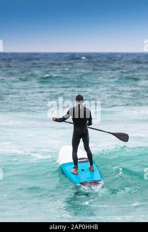 Un stand up paddle boarder voce fuori in mare a Fistral a Newquay in Cornovaglia. Foto Stock