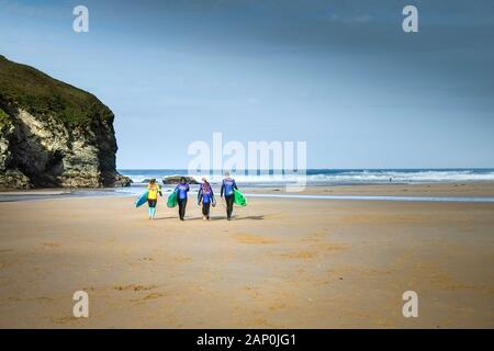 Un gruppo di surfers e loro istruttore che trasportano le loro tavole da surf su Mawgan Porth Beach a nord della costa della Cornovaglia. Foto Stock