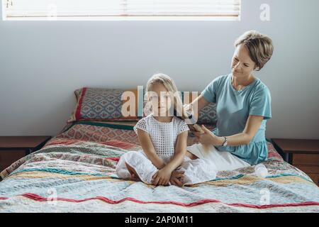 Madre fare la treccia di capelli a sua figlia sul letto Foto Stock