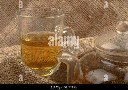 Un bicchiere di tè con motivi floreali e una teiera con tè su uno sfondo di homespun ruvida stoffa. Close up Foto Stock