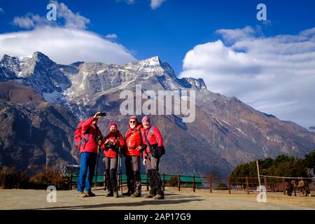 Quattro escursionisti in giacca invernale rossa stanno facendo selfie in Everest base Camp trekking con cielo blu e catena montuosa himalayana sullo sfondo Foto Stock