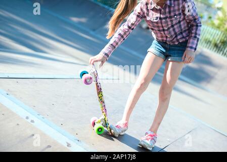 Femmina Skater corse su skateboard a skate park rampa. Giovane donna praticare lo skateboard all'aperto a skate park. Foto Stock