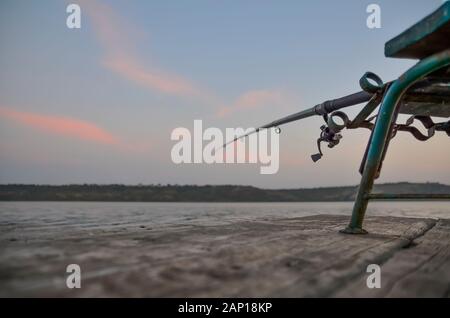 Pesca sul molo in legno su un lago di sera. Foto Stock