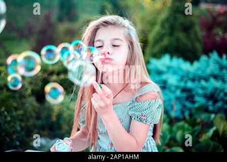 Ritratto di una bellissima bambina soffiando bolle di sapone. Un bambino gioca con bolle, su uno sfondo verde. Per esterno Foto Stock