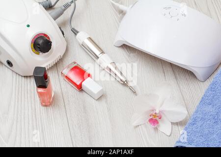 Fresa, led lampada UV, smalti per unghie e asciugamani su grigio Sfondo di legno. Una serie di strumenti di personalizzazione per hardware professionale manicure. Vista dall'alto. Foto Stock