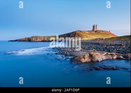 Dunstanburgh Castle e rocciosa e coperta di boulder litorale di Embleton Bay sulla costa di Northumberland Foto Stock