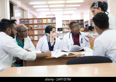 I giovani medici, razza mista. Essi siedono al tavolo, risolvere problemi medici. Le persone di sesso diverso, camici, abbigliamento medico, sono seduti ad un Foto Stock