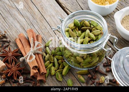 Vasetto di tutta verde i semi di cardamomo e spezie - bastoncini di cannella, cardamomo, allspices e anice su un tavolo di legno. Trattamenti Ayurveda. Foto Stock