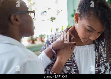 Un nero ragazza medico esamina un paziente messicano in un ufficio medici Palpates linfonodi del collo Foto Stock