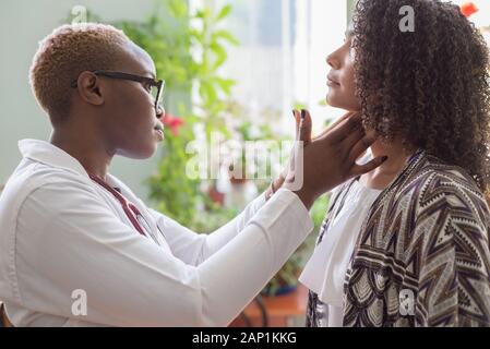 Ragazza africana in camice bianco, con un phonendoscope, indossando occhiali, esamina una messicana di un paziente con un mal di gola. Il concetto di tonsillite, s Foto Stock