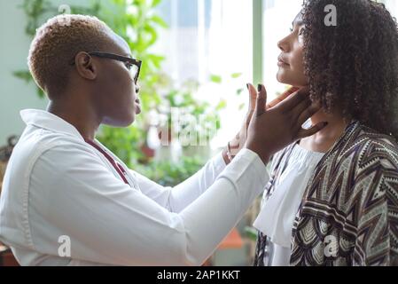 Un nero ragazza medico esamina un paziente messicano in un ufficio medici Palpates linfonodi del collo Foto Stock