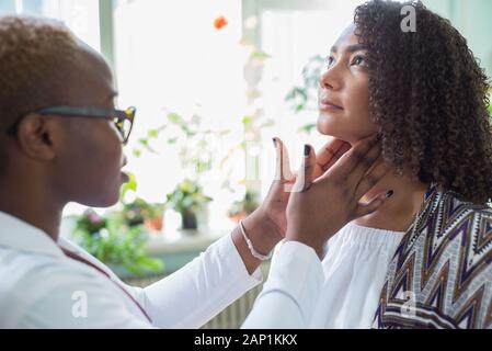 Un nero ragazza medico esamina un paziente messicano in un ufficio medici Palpates linfonodi del collo Foto Stock