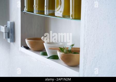 ancora vita, luminoso e soleggiato dettaglio di mensola in cucina in casa con bottiglie olio d'oliva ciotola in legno malta verde stile mediterraneo umore Foto Stock