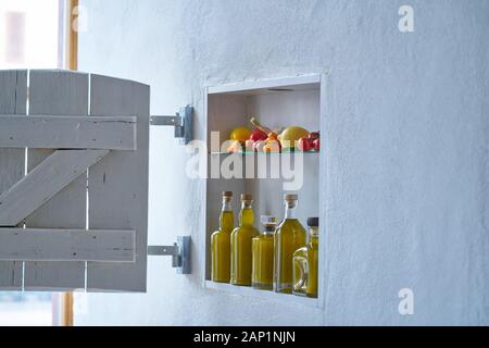 piccola mensola con serranda sul muro con bottiglie bottiglia di olio d'oliva e verdure pomodori limone paprika e aglio, vecchio appartamento casa moderno Foto Stock