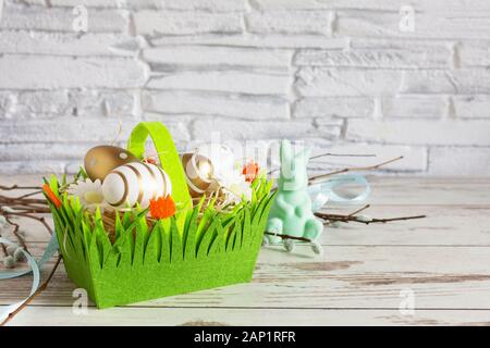 Golden colorate uova di Pasqua e il coniglietto di Pasqua in un cestello di verde. Sfondo di pasqua. Felice Pasqua tempo. Copia dello spazio. Foto Stock