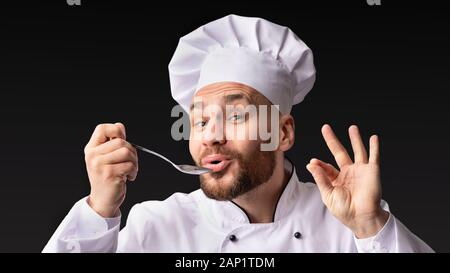 Lo Chef degustazione e approvazione di cibo cucchiaio di contenimento in posa di Studio Foto Stock